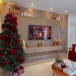 A decorated Christmas tree with red ornaments stands in a modern living room with a television.