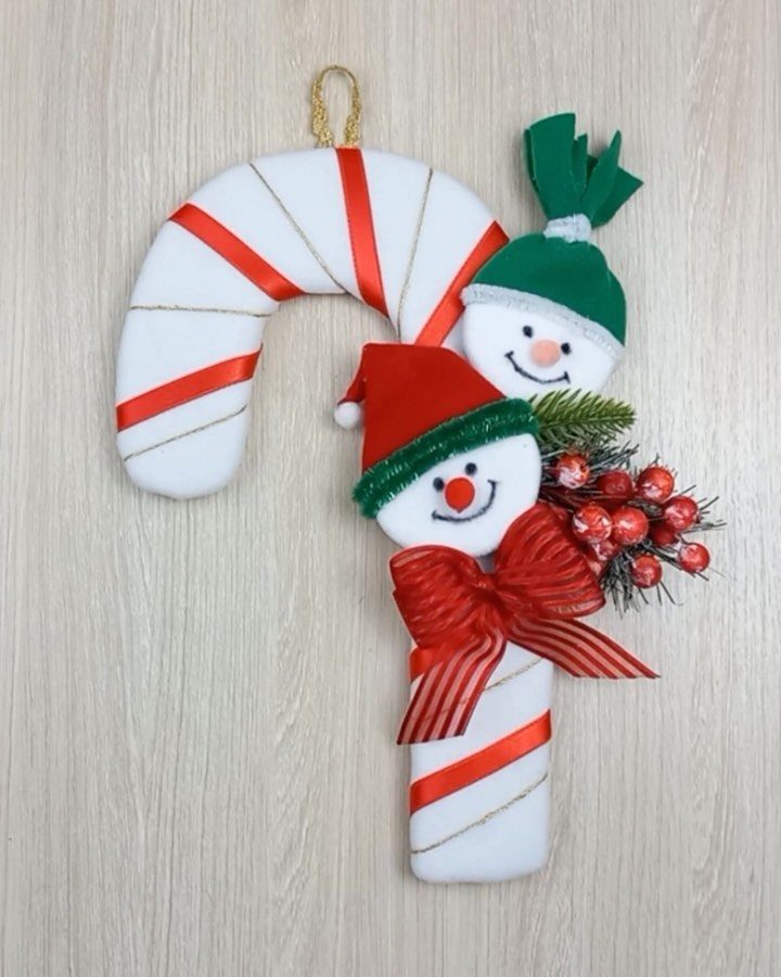 A candy cane shaped ornament featuring two small snowman faces with red and green hats.