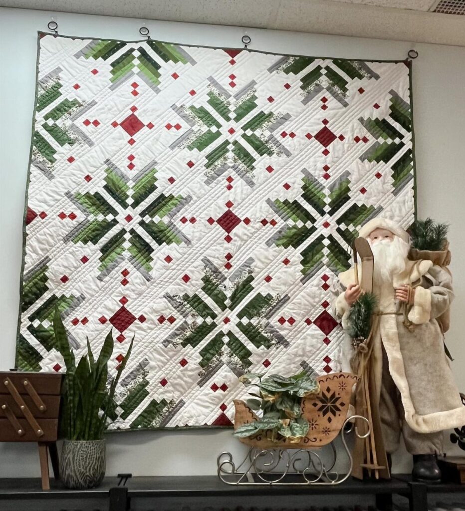 A white quilt with green and red star patterns hanging on a wall above festive decorations.