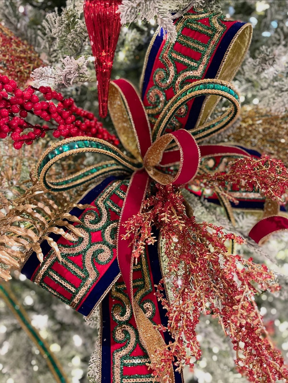 A large decorative red and gold patterned ribbon bow on a snowy Christmas tree.