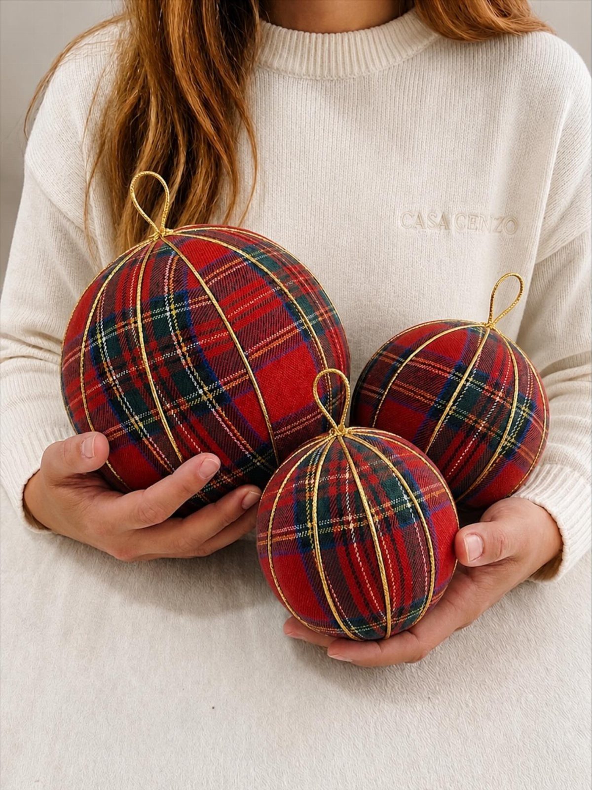 Three red and green plaid flannel Christmas ornaments held in a person's hands.