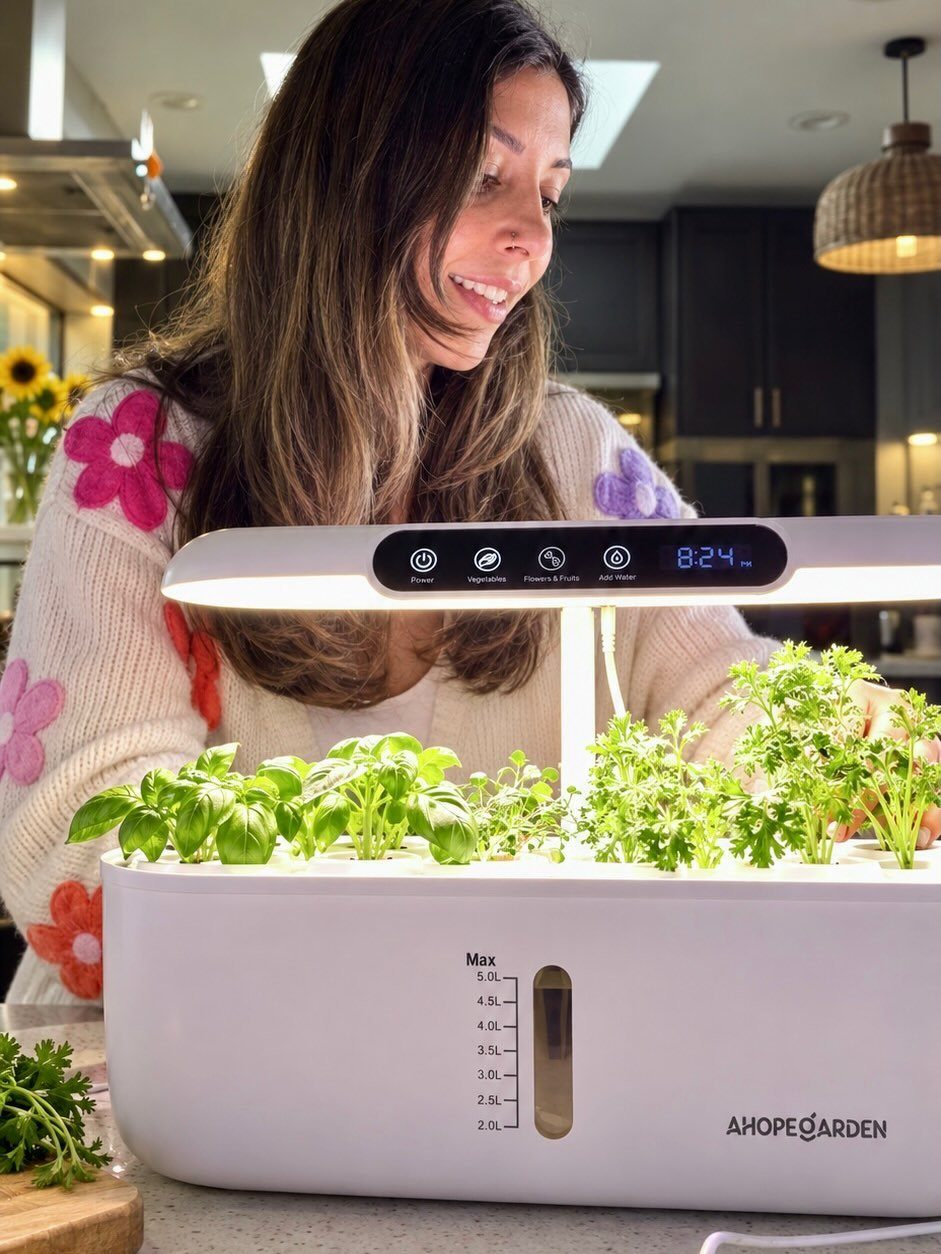 A woman smiling at a white smart indoor garden with integrated grow lights and green plants.