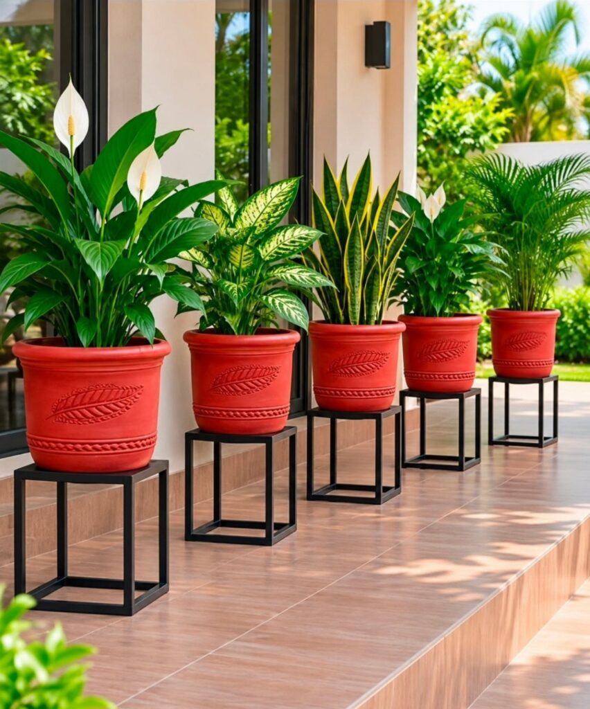 Red decorative plant pots with green foliage arranged on black metal stands on a patio.